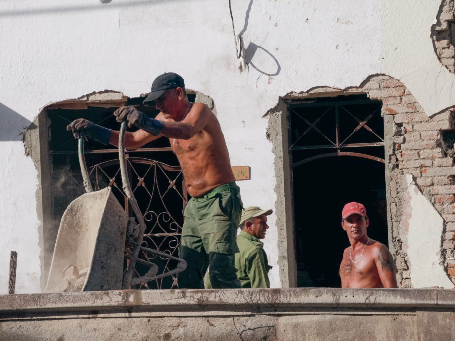 Três trabalhadores atuam em uma obra de reforma de um edifício, sob a luz do sol.