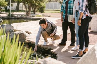 Grupo de estudantes participa de atividade de estudo junto a um lago, observando elementos da natureza.