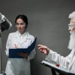 Pesquisadores de jaleco e óculos de proteção analisam uma tecnologia robótica em um laboratório.