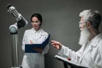 Pesquisadores de jaleco e óculos de proteção analisam uma tecnologia robótica em um laboratório.